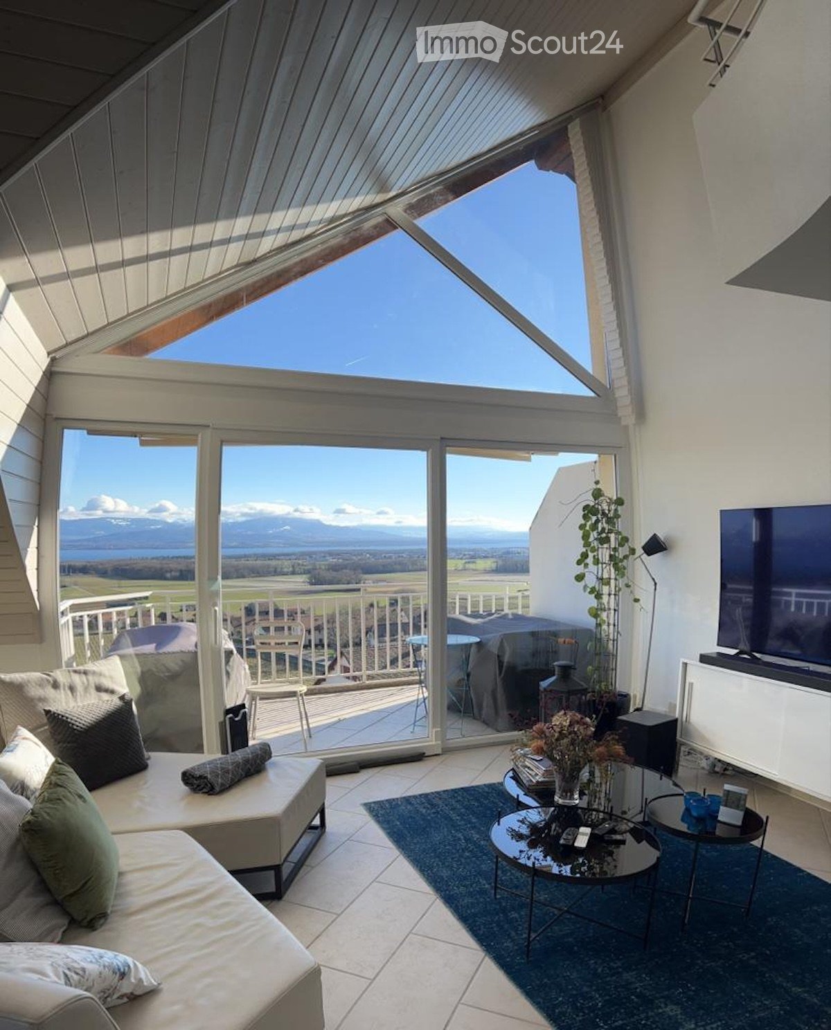 Bright living room with large windows and a view, featuring a sofa, coffee table, and television.