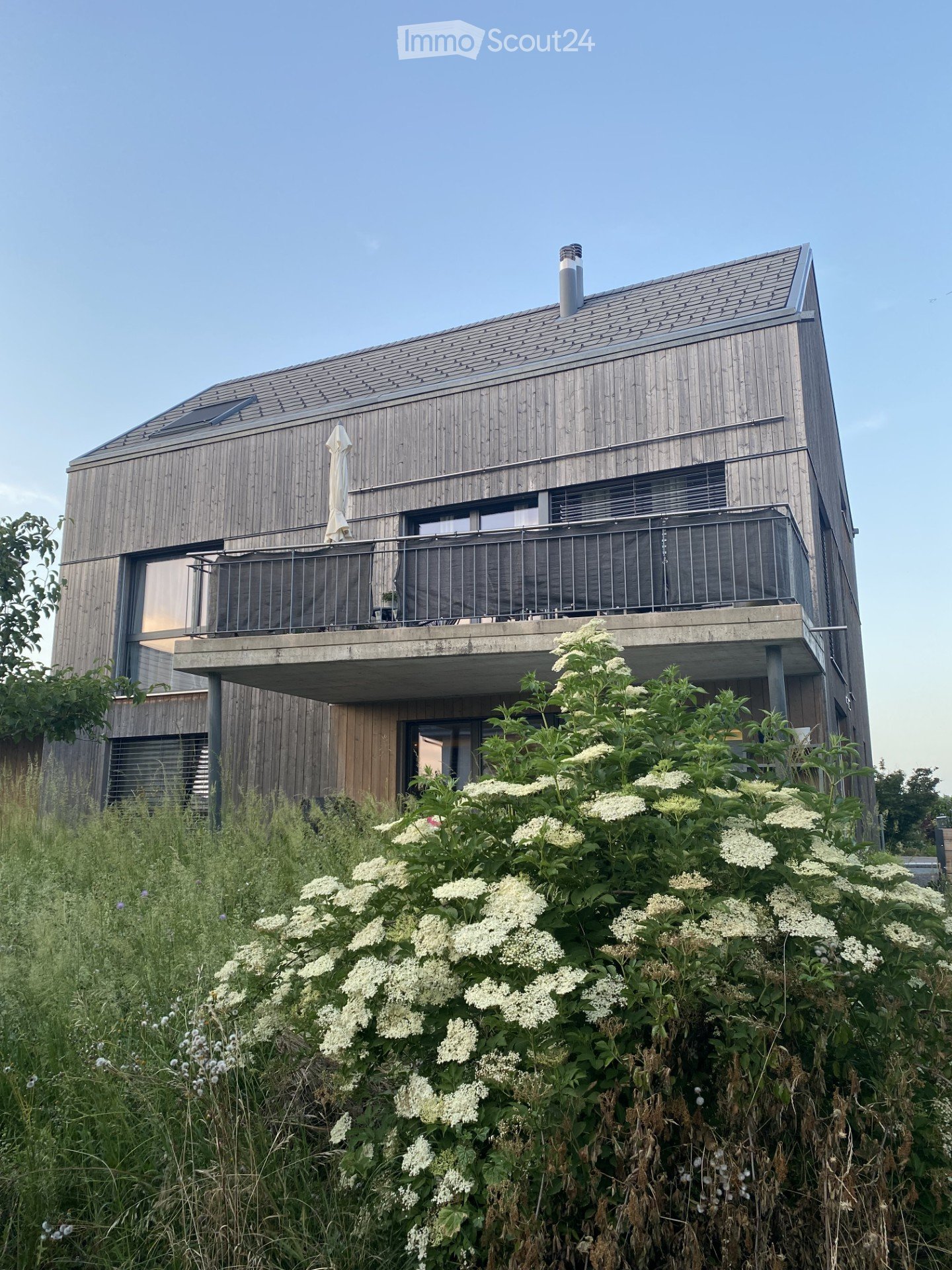 Modern two-story house with wooden facade, large windows, and a balcony with a railing.
