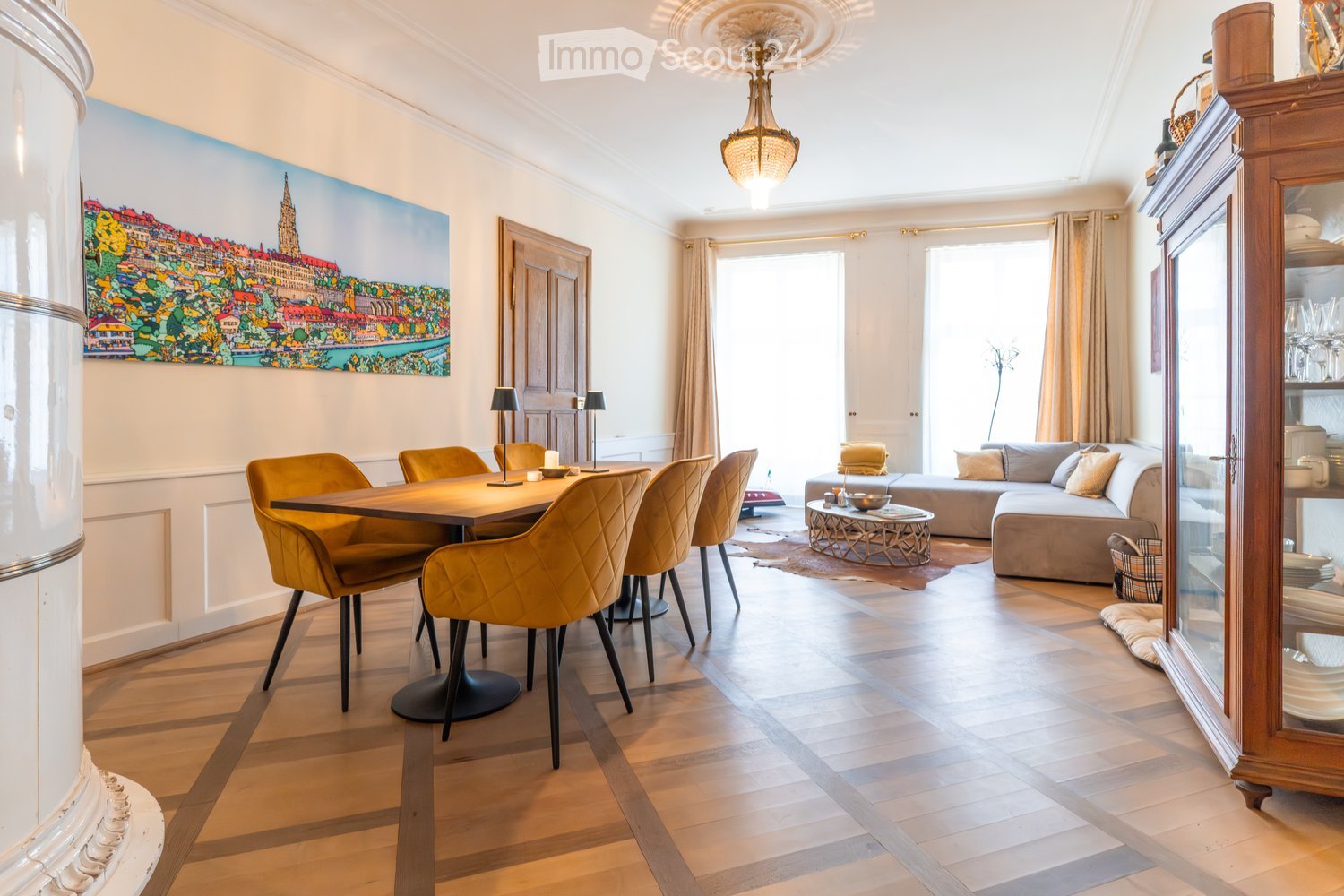 Open-plan living and dining area with wooden flooring, a large sofa, a coffee table, a dining table with chairs, and a cabinet with glass doors.