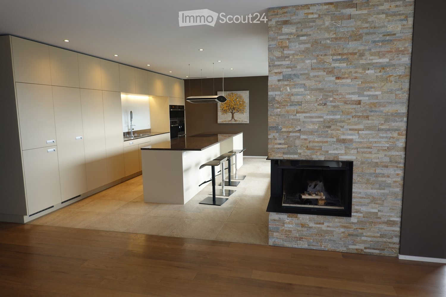 Modern kitchen with a stone fireplace, kitchen island with bar stools, sleek cabinetry, and a contemporary faucet.