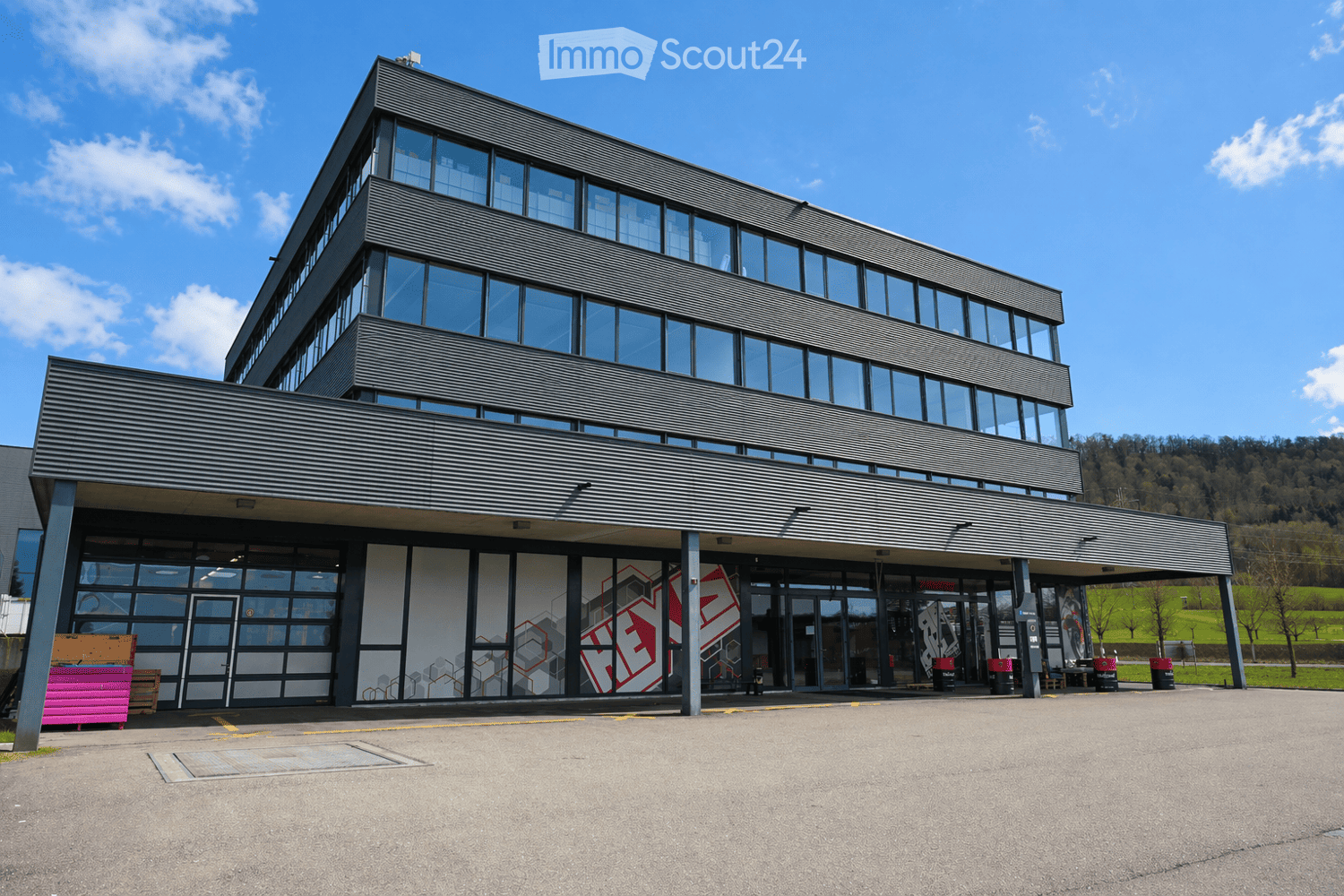 Modern two-story building with large glass windows and a sleek, angular design. The entrance features a covered walkway with geometric wall art.