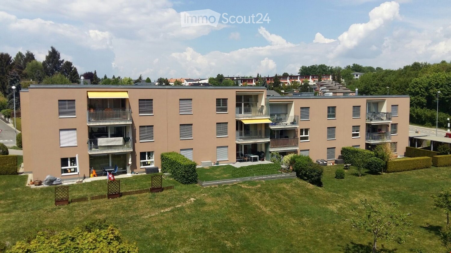 Multi-story residential building with balconies, surrounded by a well-maintained lawn and trees.