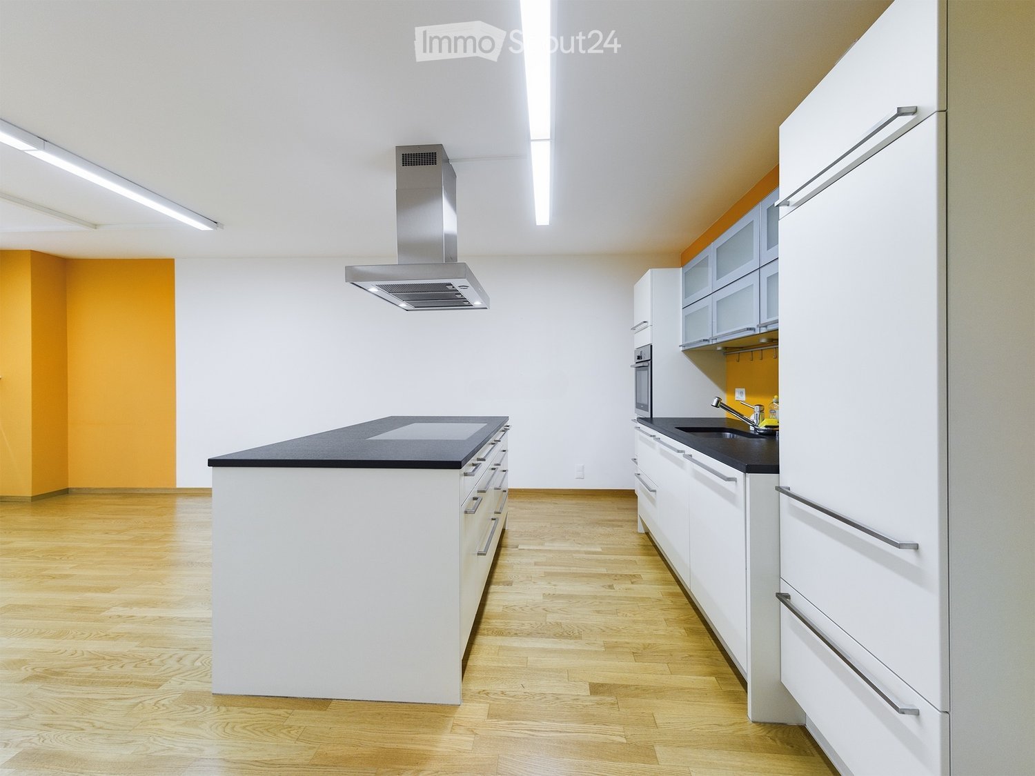 Modern kitchen with white cabinets, black countertops, wooden flooring, and stainless steel appliances including a range hood and oven.