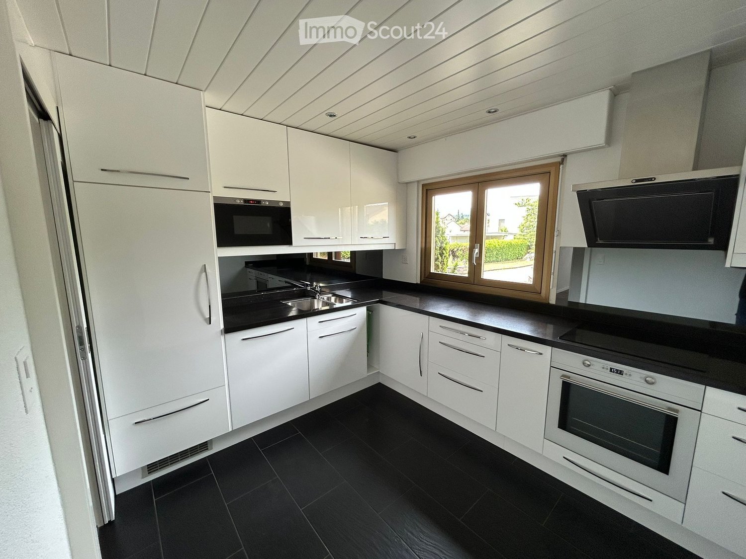 Modern kitchen with white cabinets, black countertops, stainless steel appliances, and a large window offering a view of the outside.