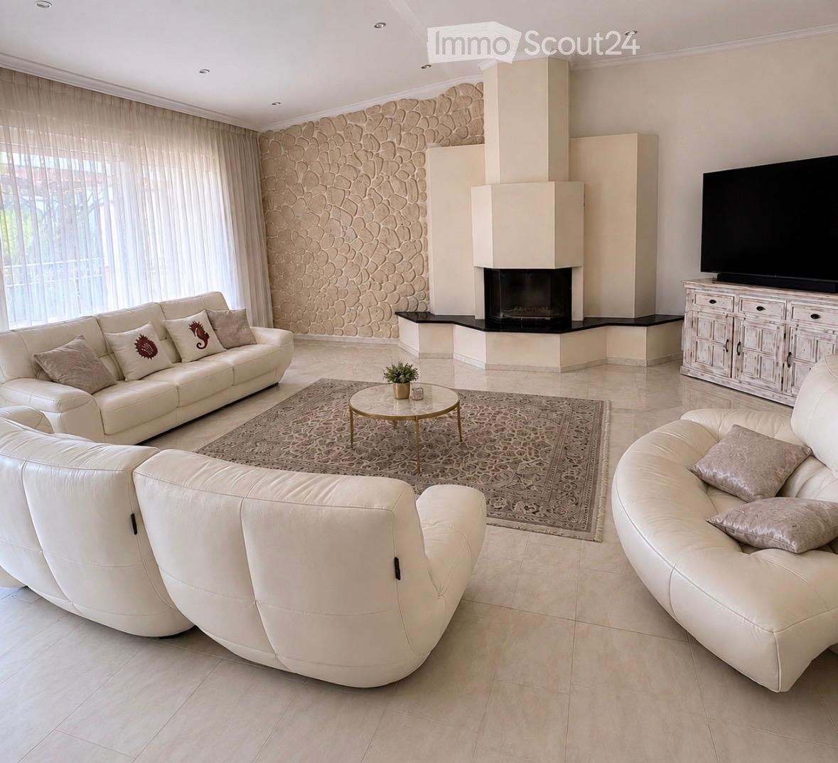 Modern living room with white leather sofas, a fireplace, a coffee table, and a television on a cabinet.