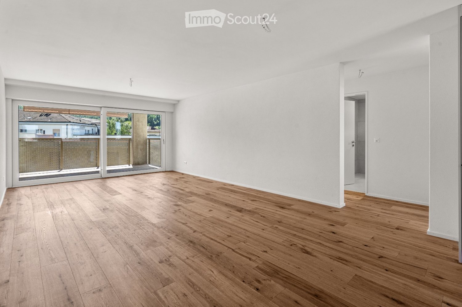 Empty room with light wooden flooring, white walls, and large sliding glass doors leading to a balcony.