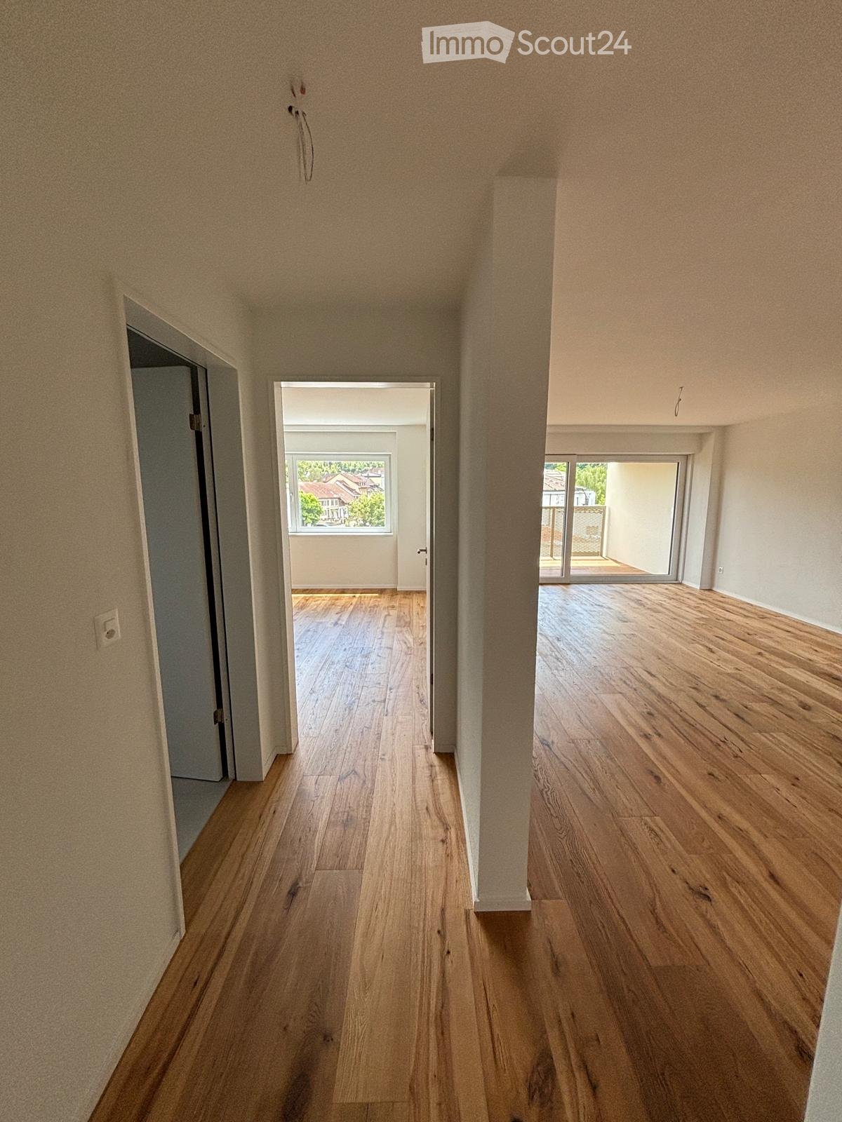 Empty hallway with wooden flooring, beige walls, and multiple doors leading to other rooms and outdoor areas.