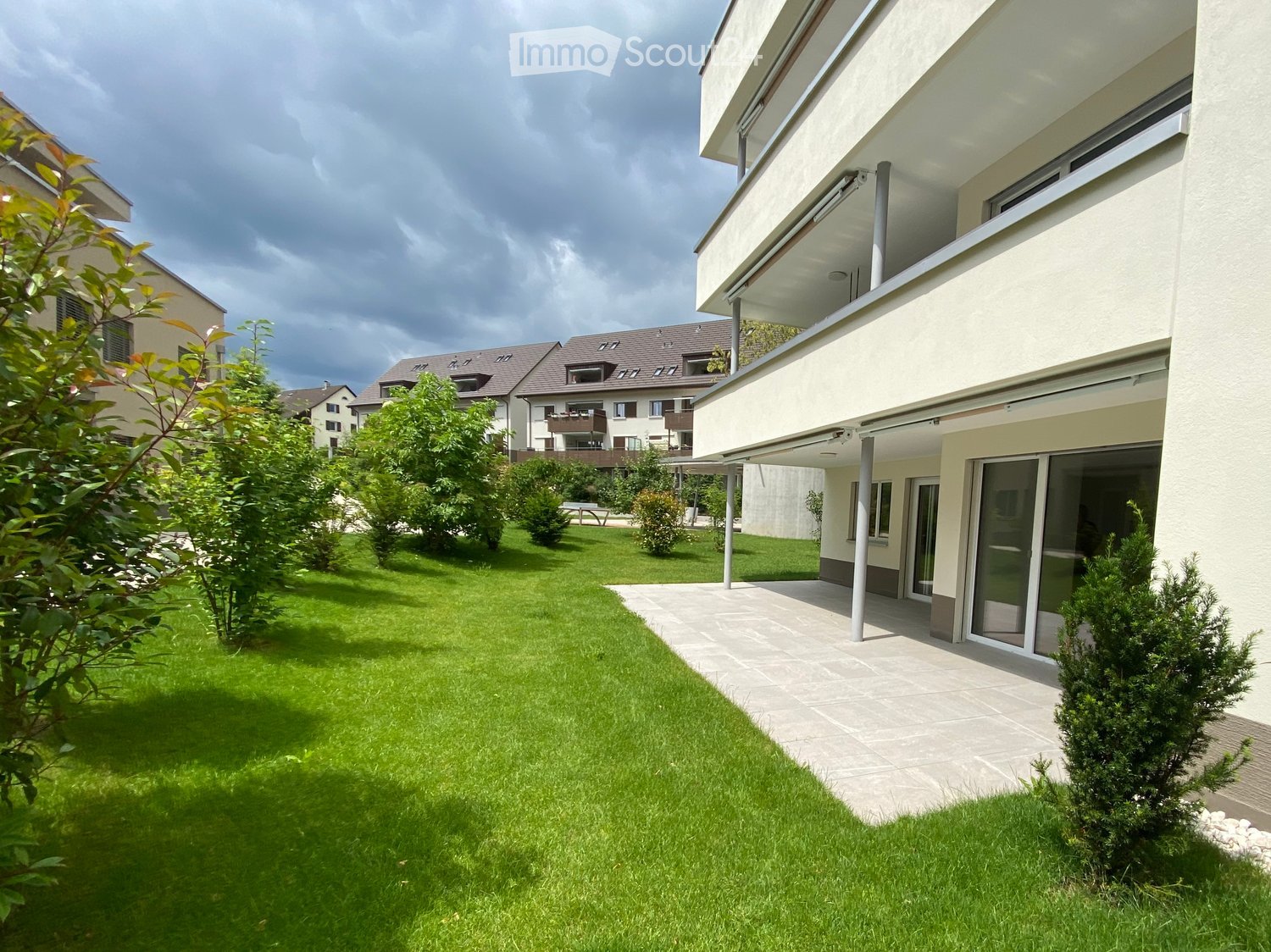 Well-maintained garden with green lawn, trimmed bushes, and a modern house with large windows and a balcony.