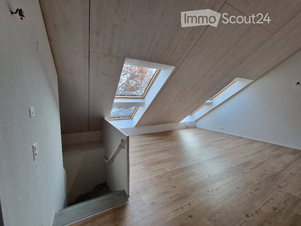 Empty room with wooden flooring, white walls, and skylight windows allowing natural light. Staircase leads to another level.