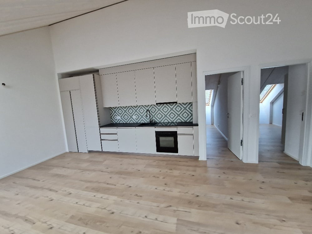 Empty kitchen with white cabinets, a black countertop, and a geometric tile backsplash. The floor is made of light wooden planks.