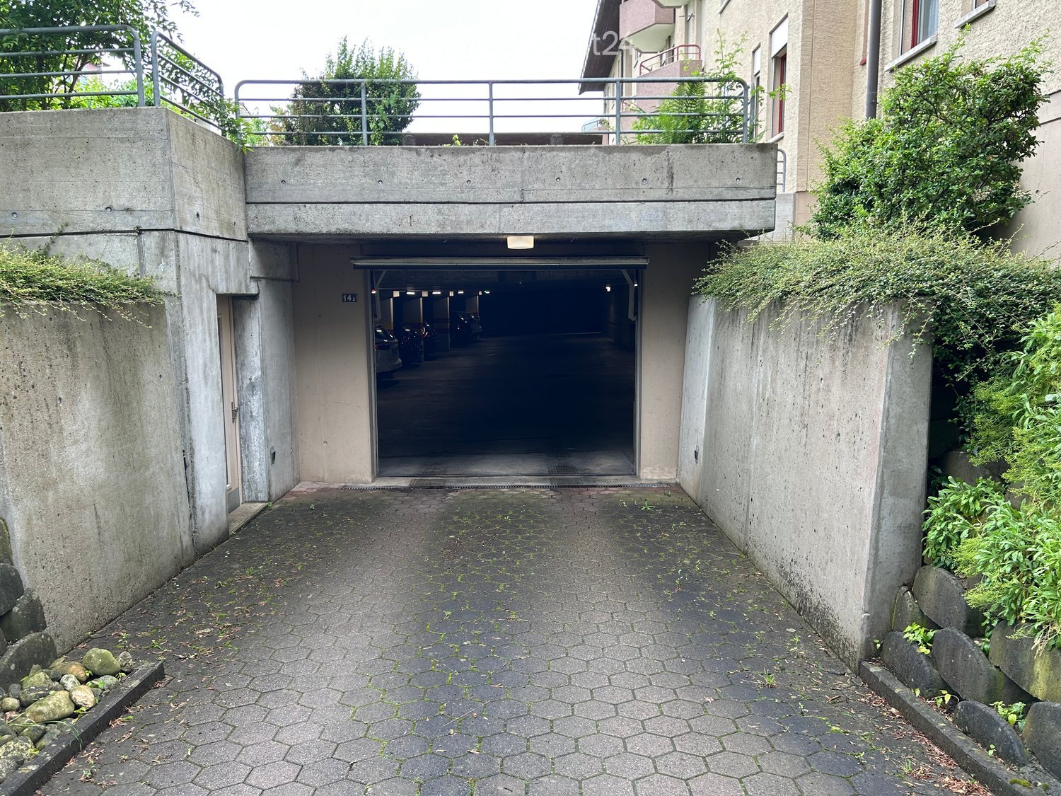 Entrance to a multi-story parking garage with a concrete structure, metal railing, and greenery on the sides.