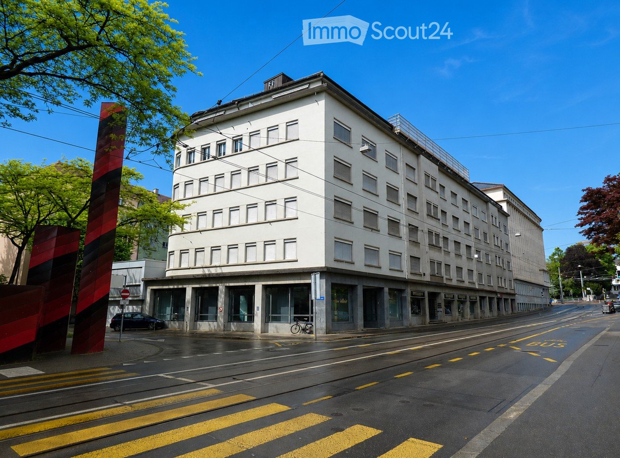 Multi-story building with white facade, multiple windows, and a flat roof, located on a street with tram tracks and a bus lane.