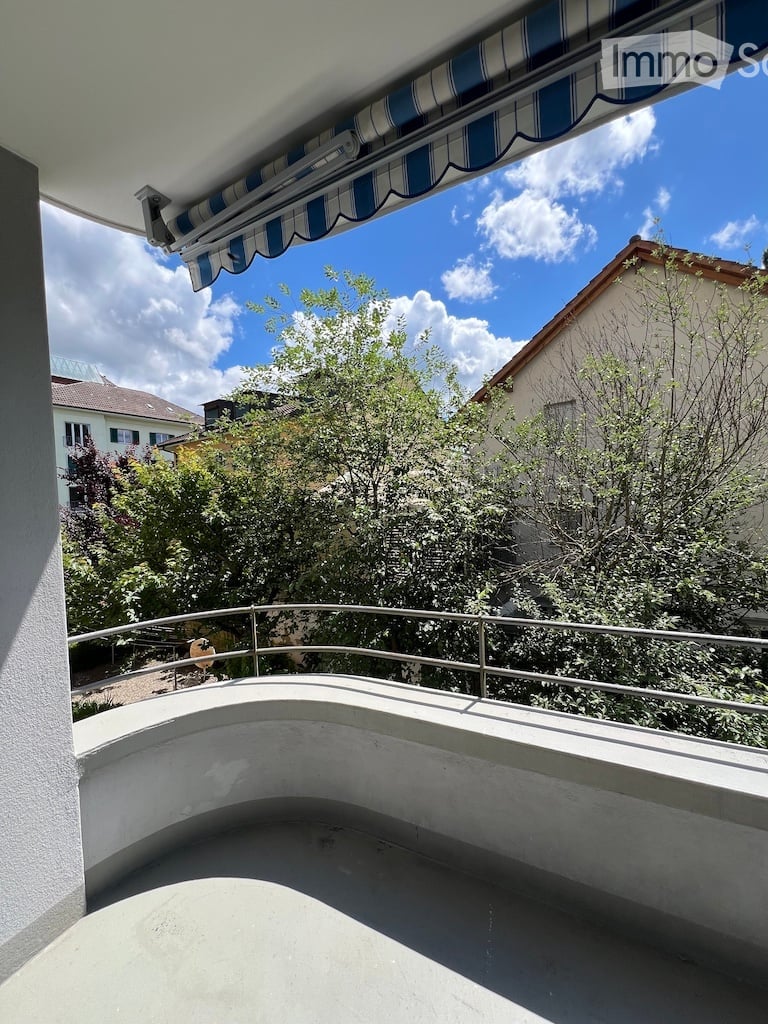 Balcony with a striped awning, metal railing, and view of trees and neighboring houses.