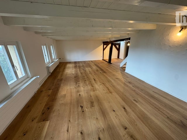 Completely empty room with wooden flooring, white walls, and large windows. No furniture or equipment.
