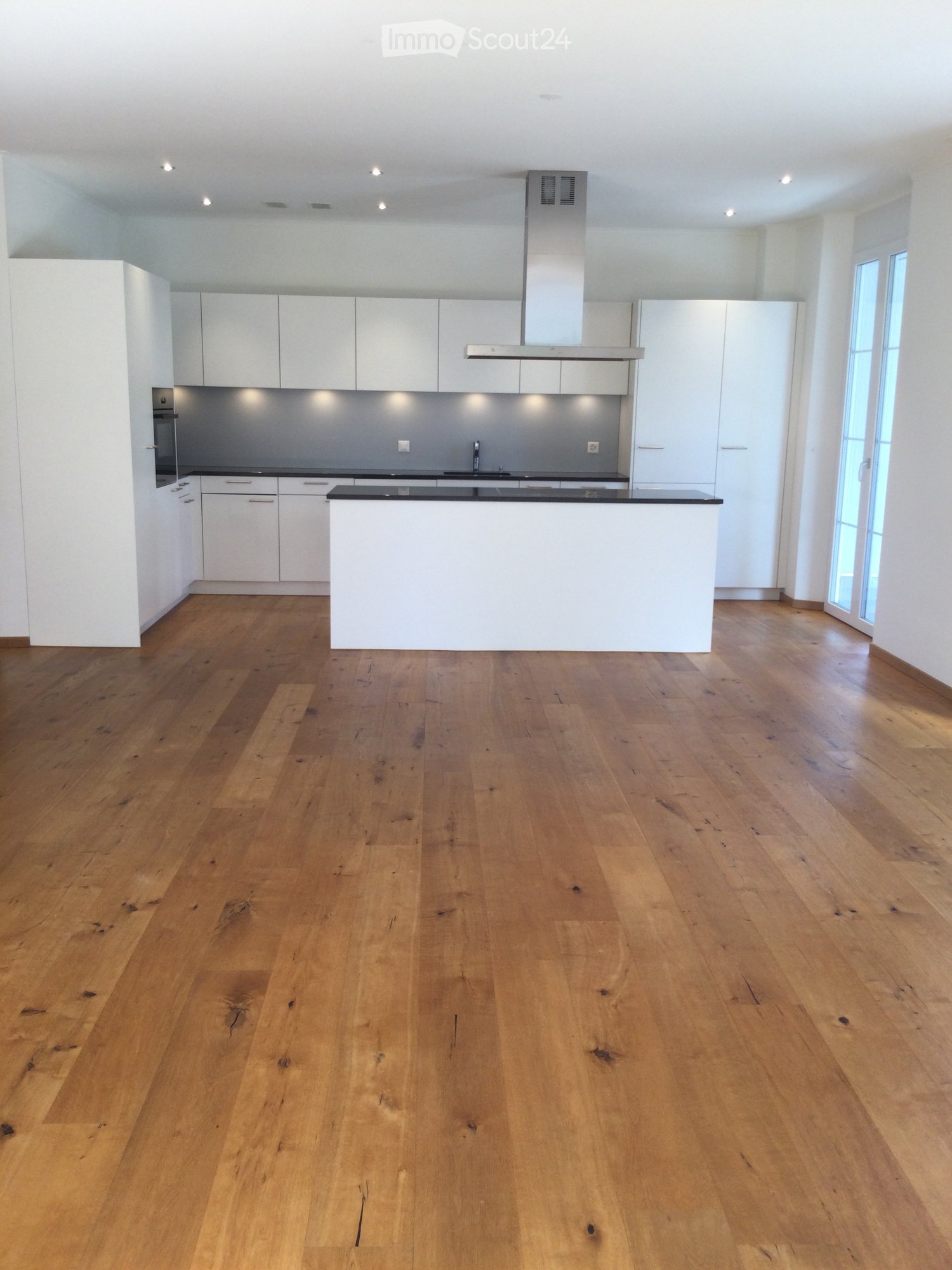 Empty kitchen with white cabinets, a central island, and wooden flooring.