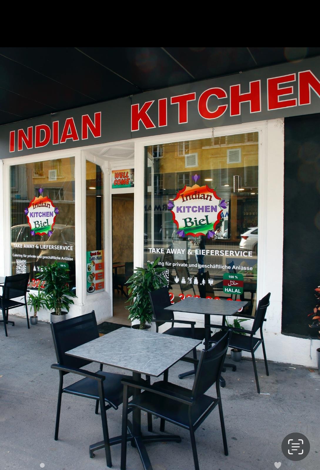 Outdoor seating area of an Indian restaurant with tables, chairs, and potted plants.