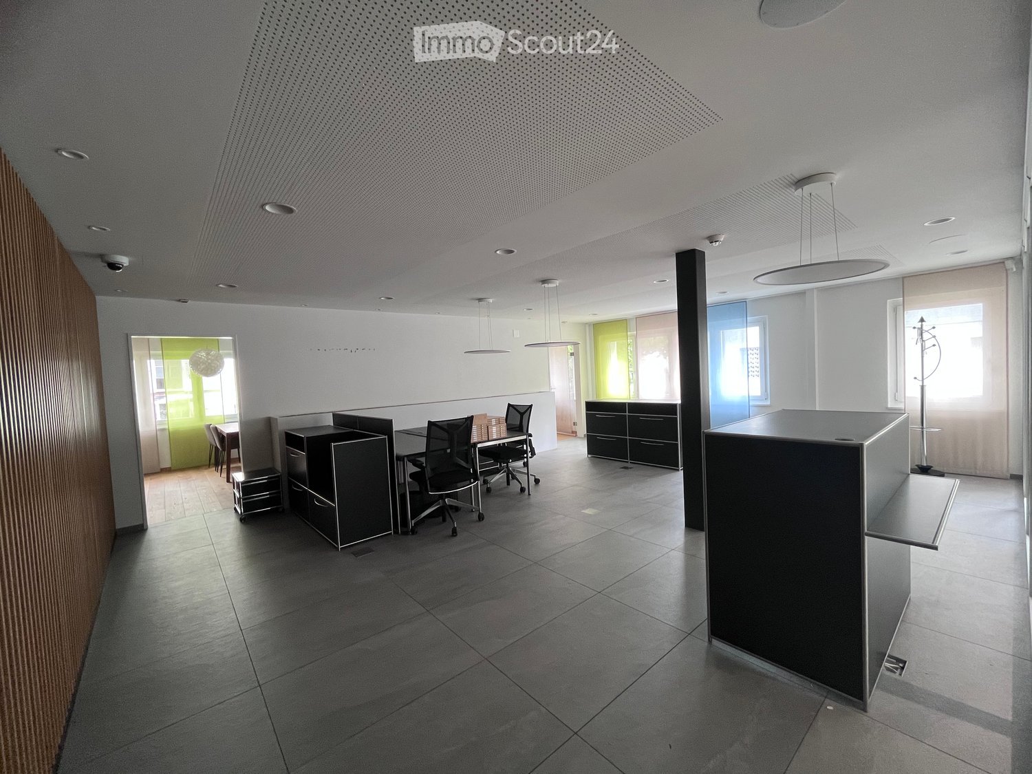 Modern office space with grey tiled floor, white walls, and black furniture including desks, chairs, and cabinets.