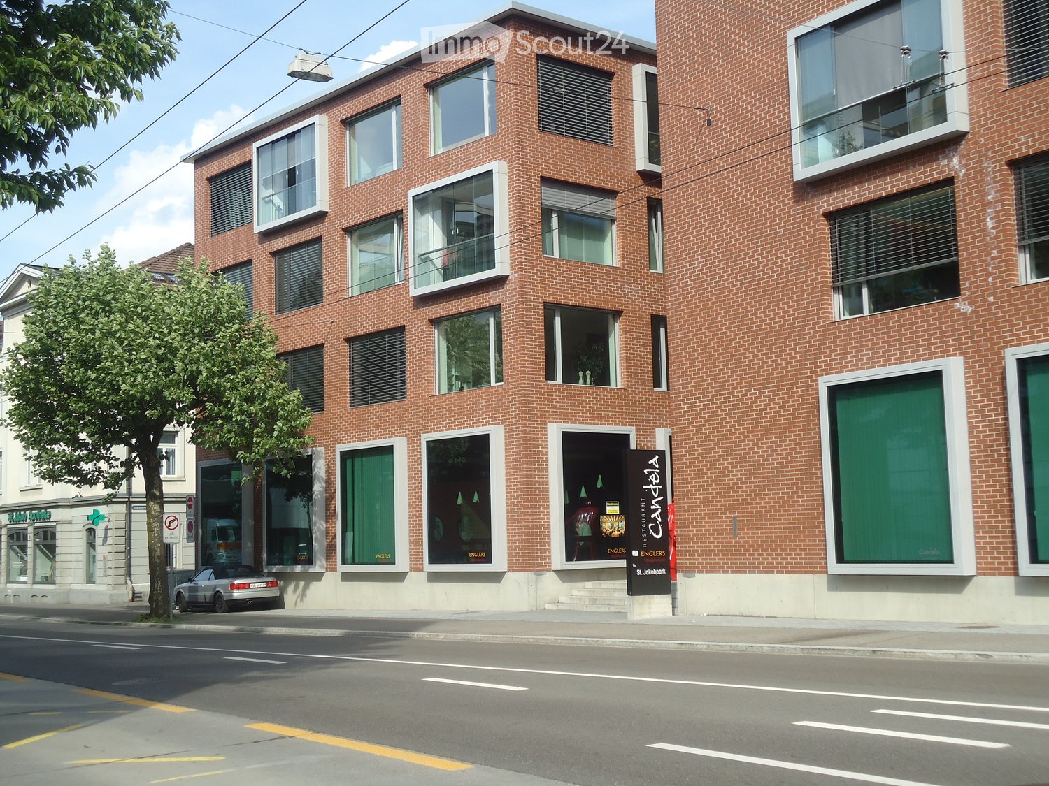 Four-story brick building with large windows and balconies, featuring a restaurant sign for "Candelá" on the ground floor.