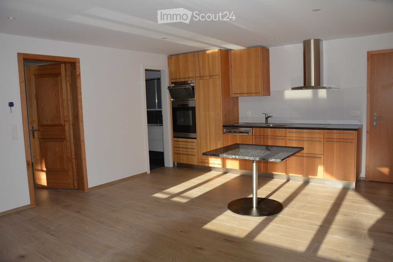 Modern kitchen with wooden cabinets, granite countertop, built-in oven, sink, and a round table with a metal base.