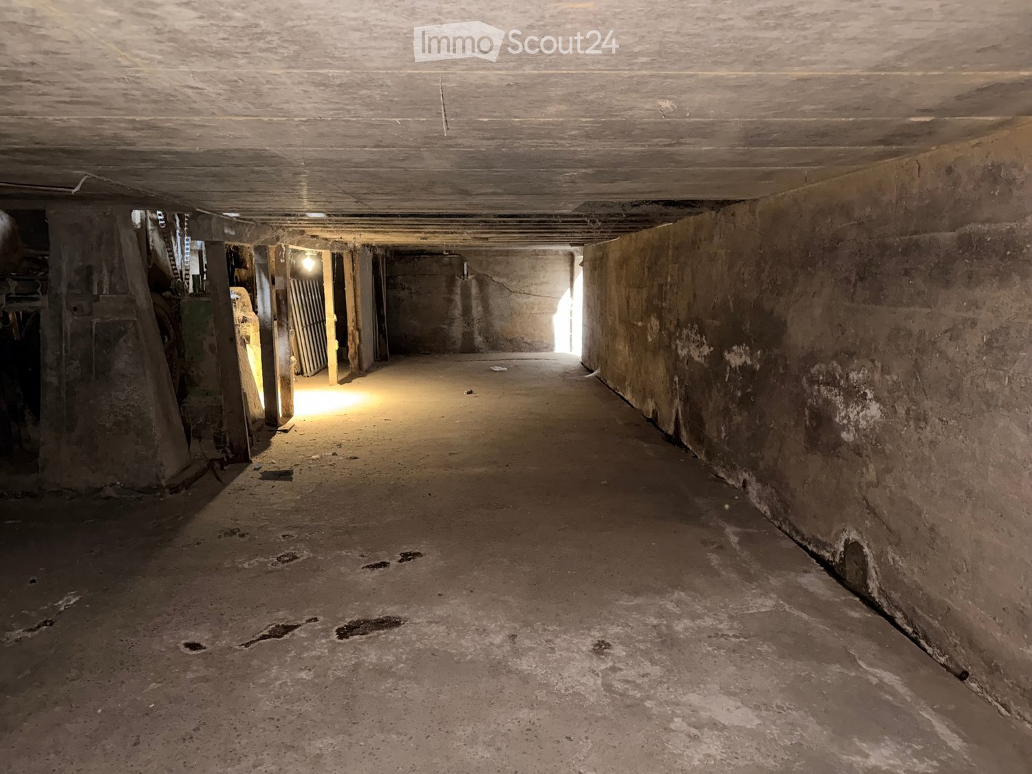 Empty, dimly lit corridor with concrete walls and floor, featuring a series of doors and pillars on the left side.