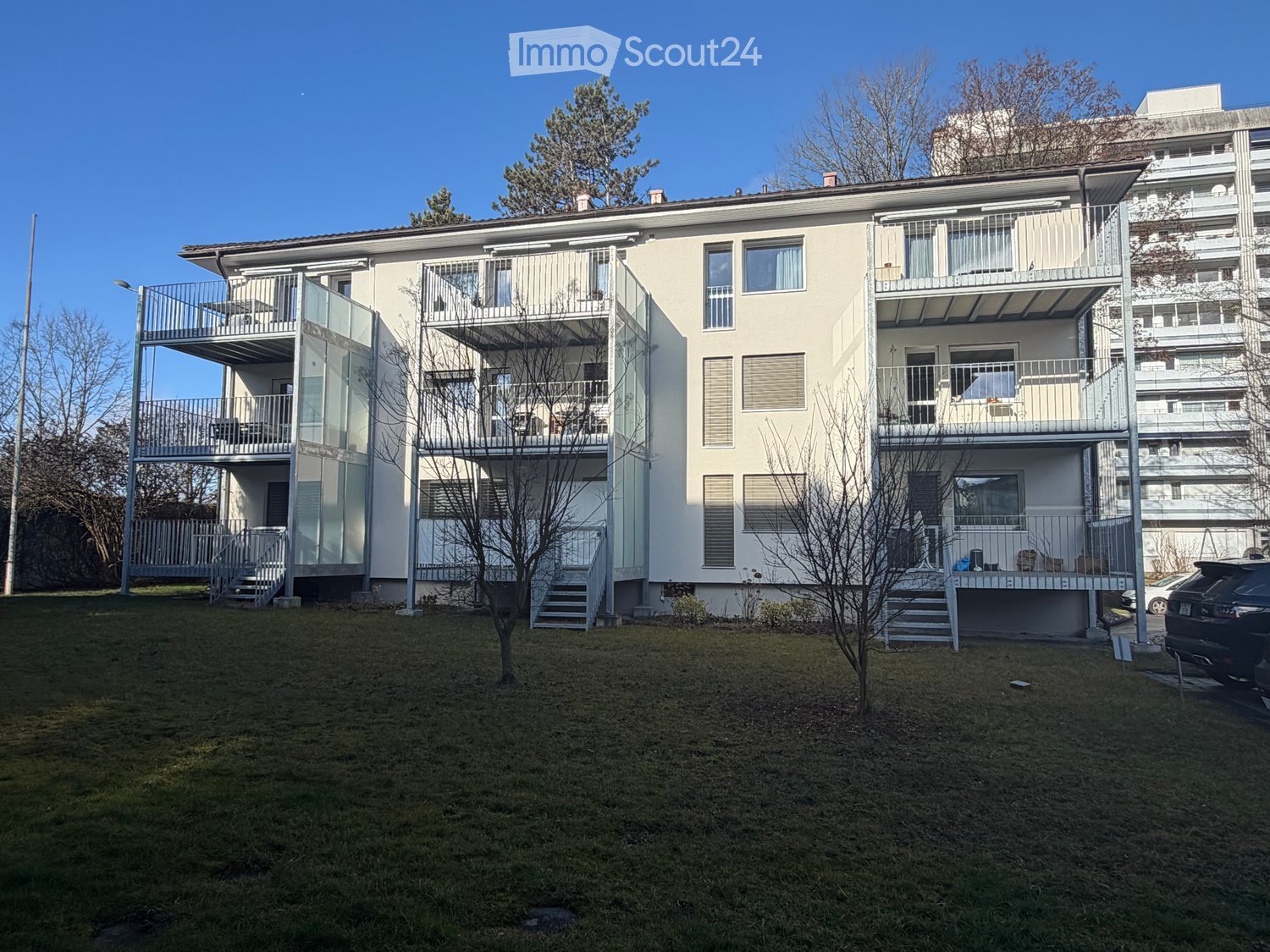 Modern two-story residential building with balconies, glass railings, and a small front lawn.