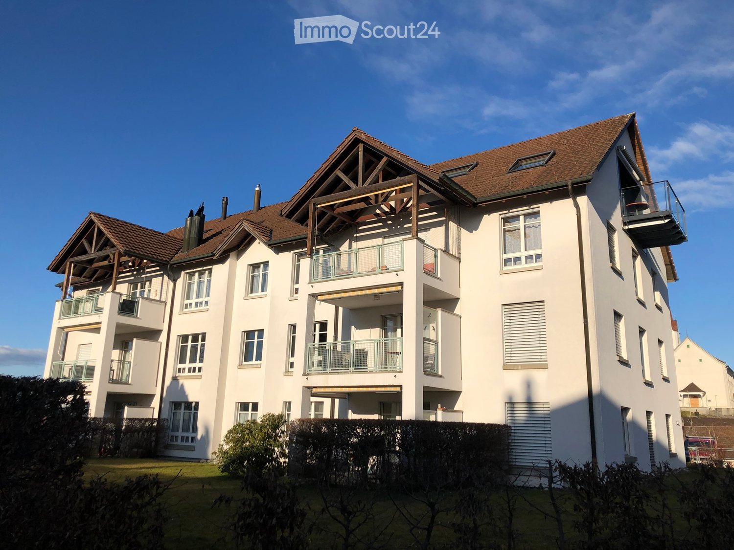 modern apartment building, white walls, brown roof, multiple balconies, chimneys
