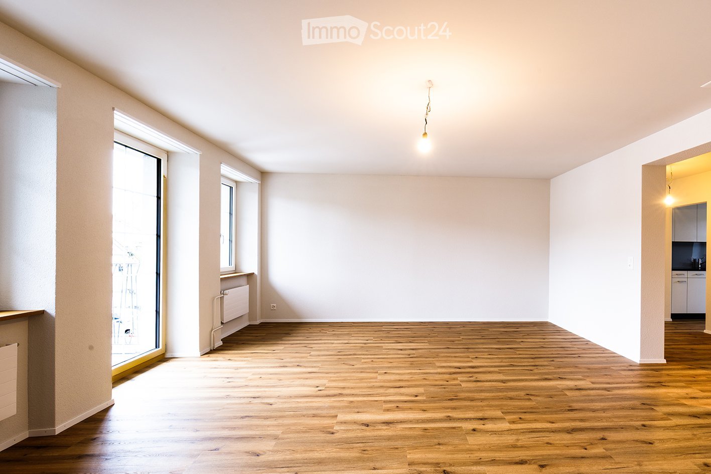 Empty room with wooden flooring, white walls, and large windows allowing natural light. No furniture or equipment is present.