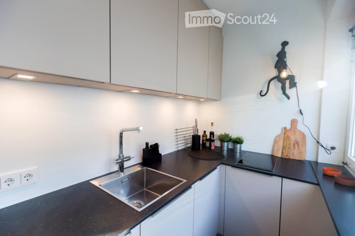 Modern kitchen with white cabinets, black countertops, stainless steel sink, and various small appliances and decor items.