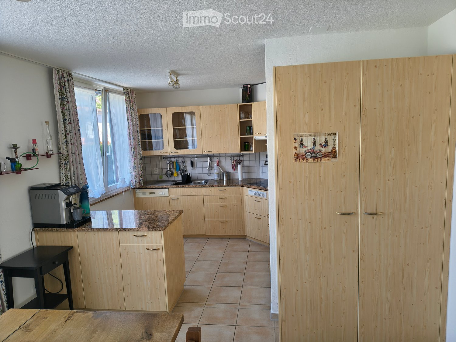 Bright kitchen with light wooden cabinets, granite countertop, and tiled floor. Features a coffee maker, sink, and various kitchen utensils.