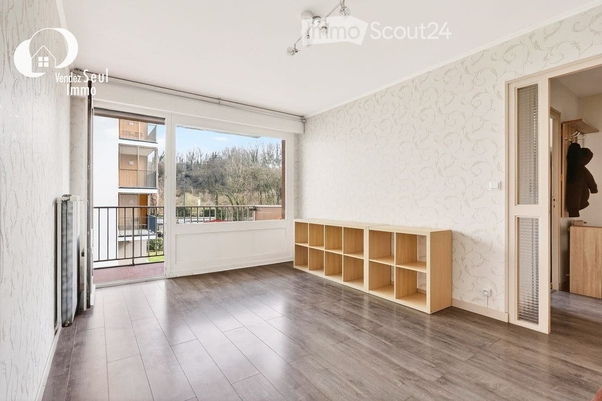 Empty room with wooden flooring, large window with balcony access, and a small wooden shelving unit.