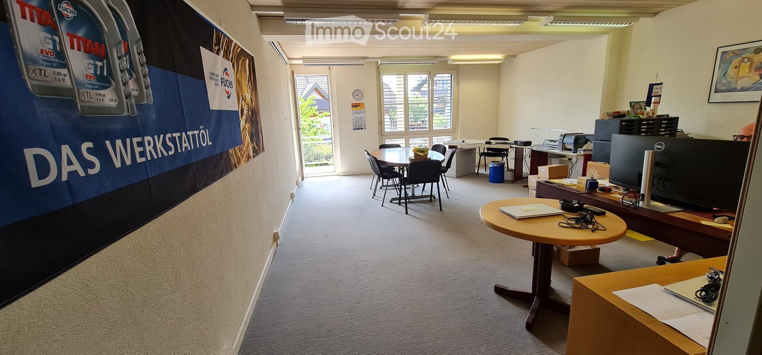 Office space with a round table, chairs, laptop, computer screen, printer, and clock on the wall.