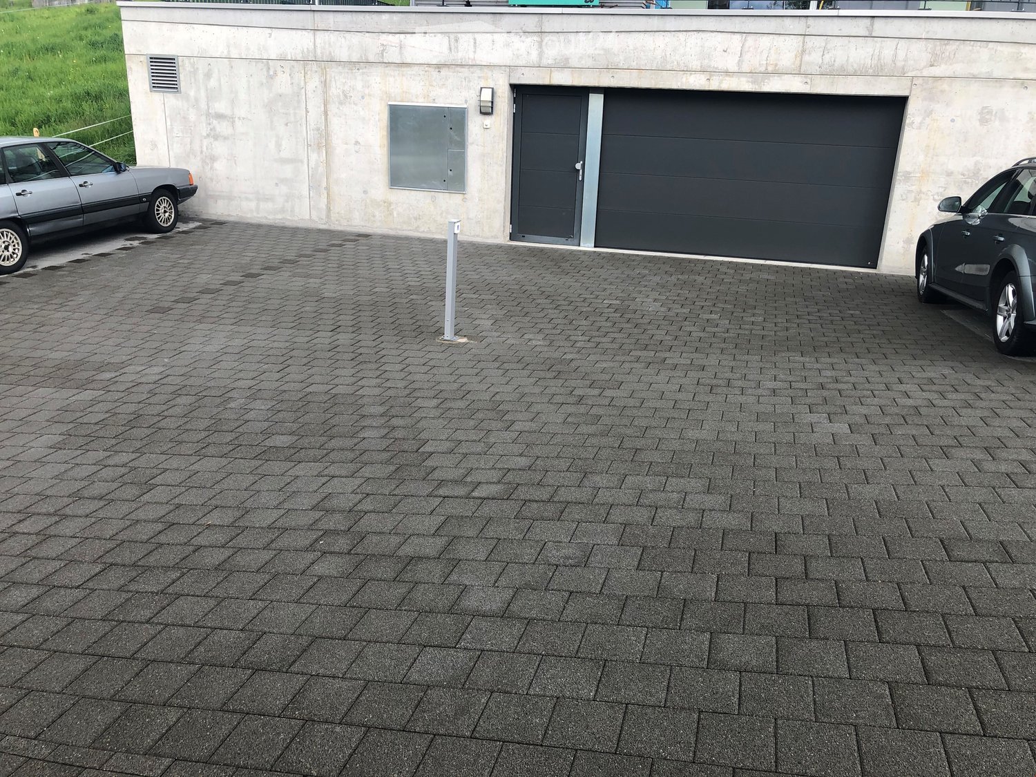 Modern building with a large garage door, two parked cars, and a paved driveway.