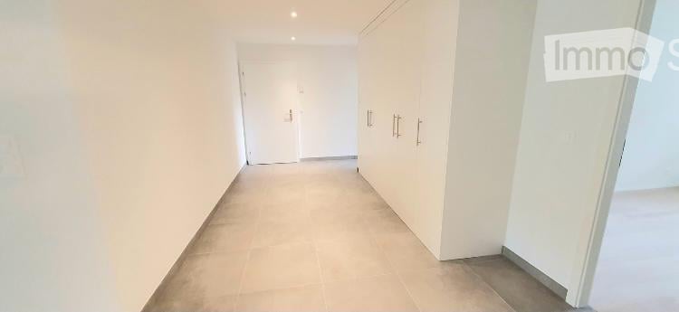 Empty hallway with white walls, tiled floor, and built-in white closet with silver handles.