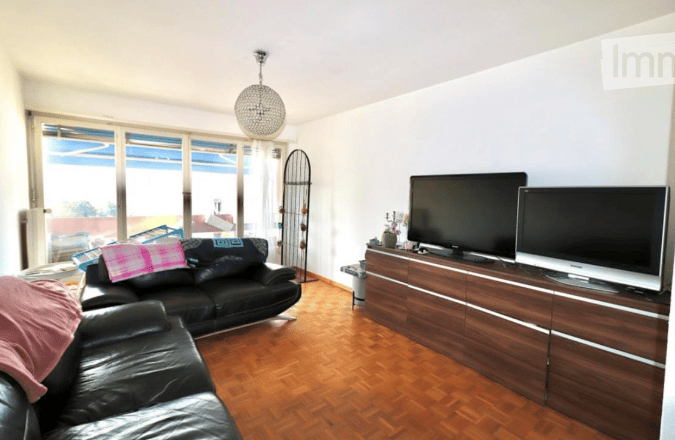 Modern living room with large windows offering a view, featuring a black leather sofa, a wooden coffee table, a flat-screen TV, and a floor lamp.