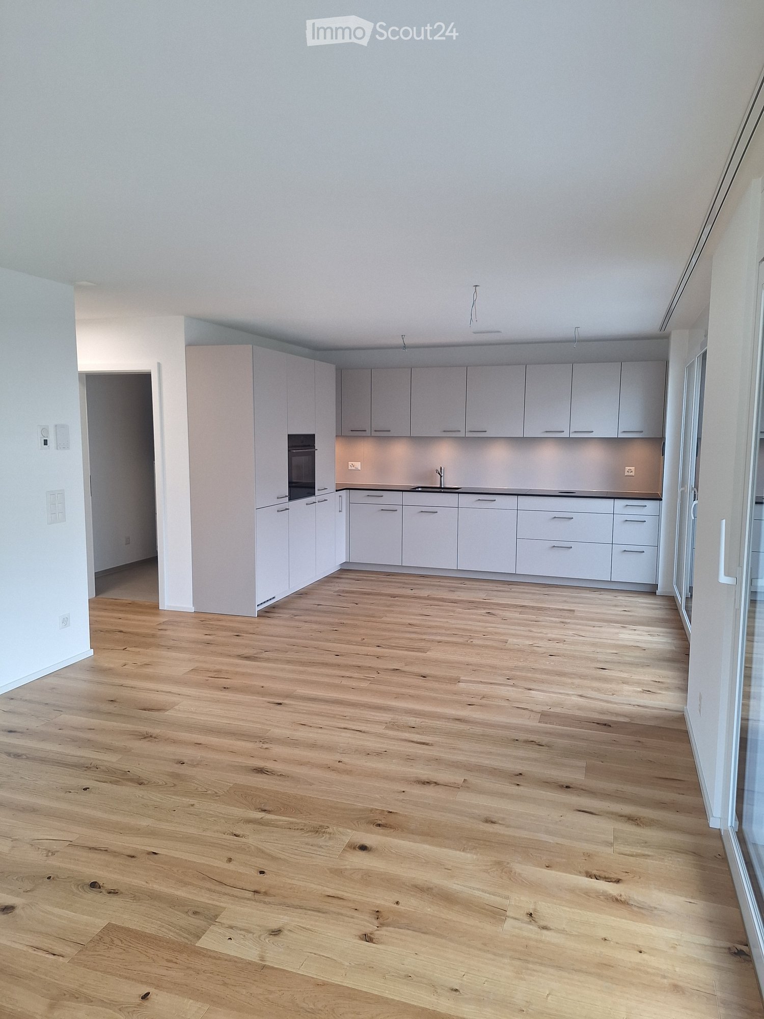 Empty kitchen with light grey cabinets, wooden floor, and built-in appliances including an oven and sink.
