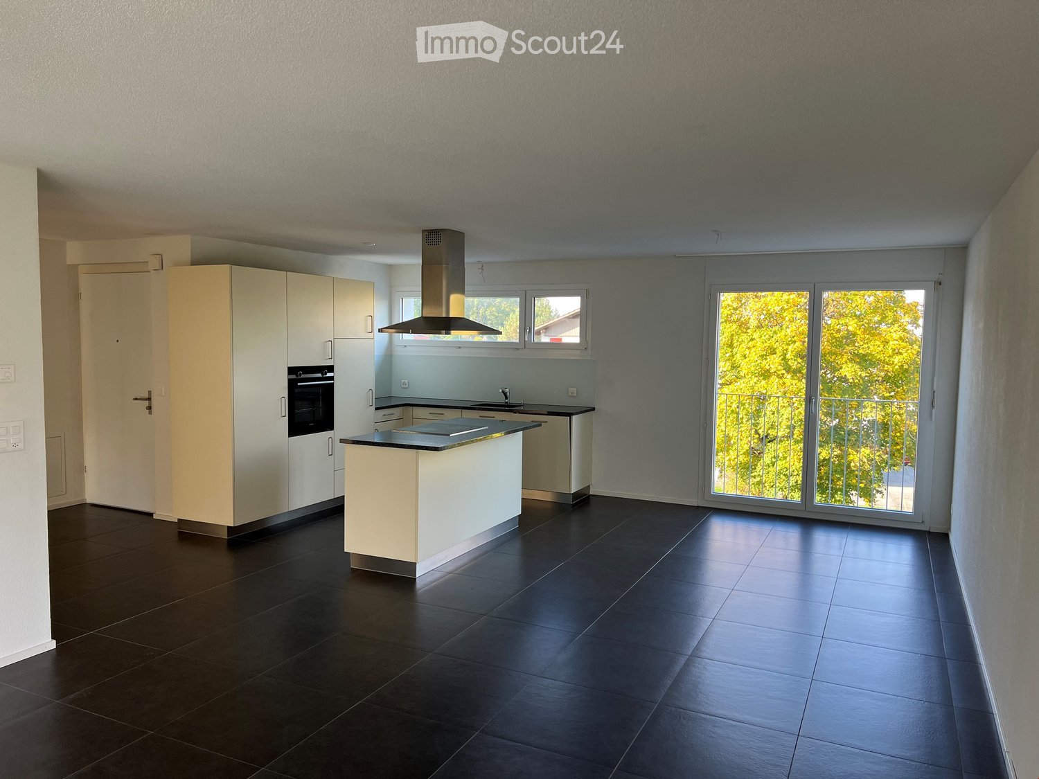 Modern kitchen with white cabinets, black tiled floor, central island, and large windows overlooking a balcony.