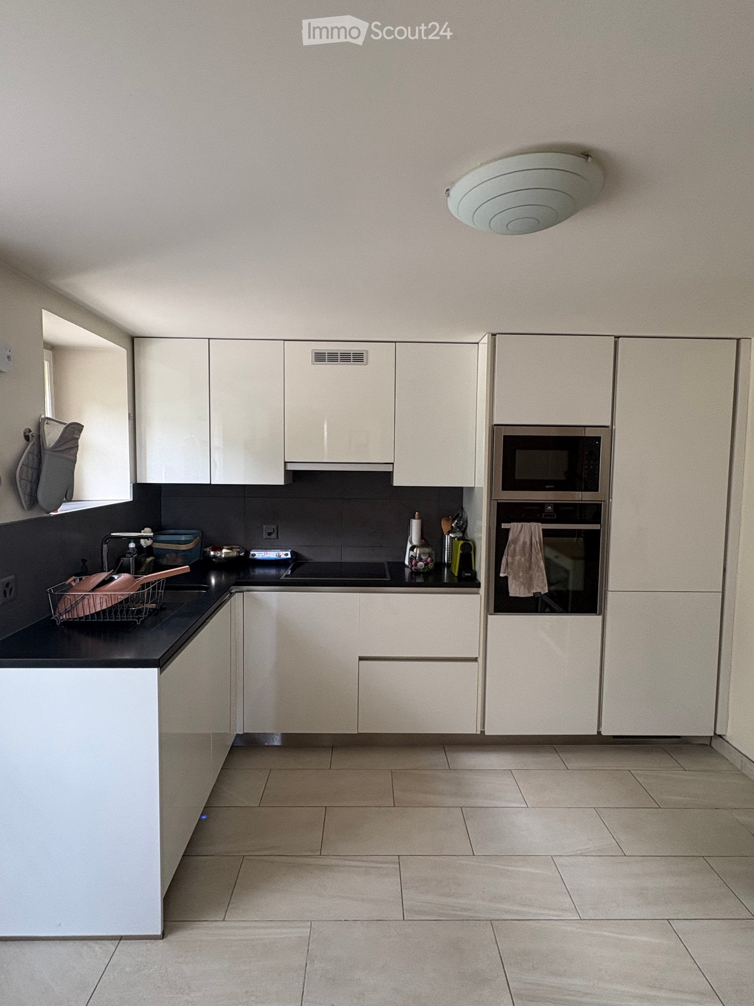 Modern kitchen with white cabinets, stainless steel appliances, black countertop, and tiled floor.