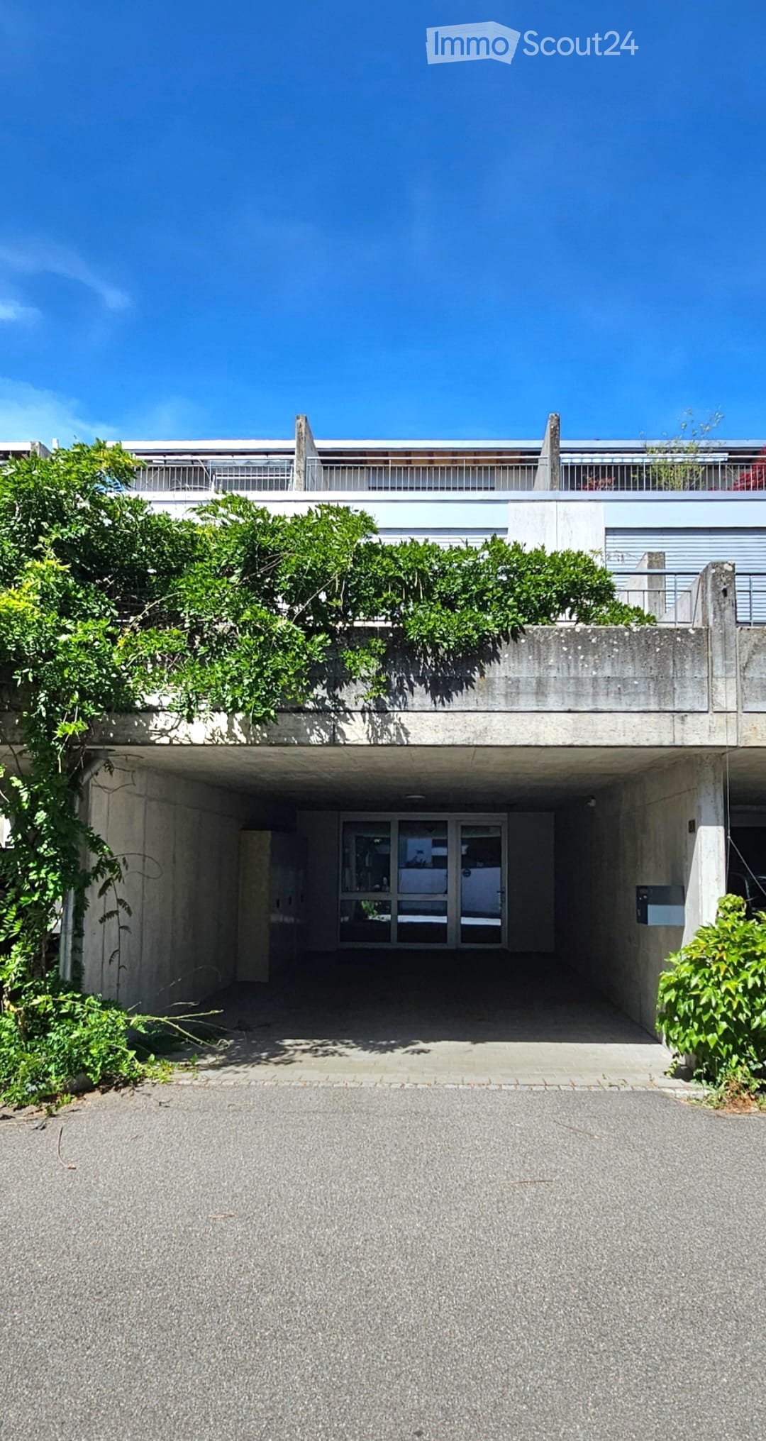Modern concrete building with a covered entrance, greenery on the roof, and a spacious driveway.