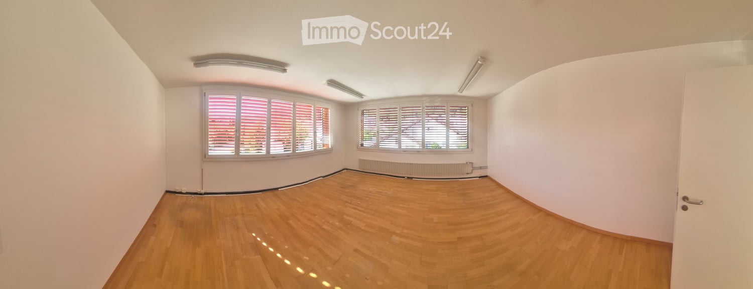 Empty room with wooden flooring, white walls, large windows with shutters, and a radiator below one window.
