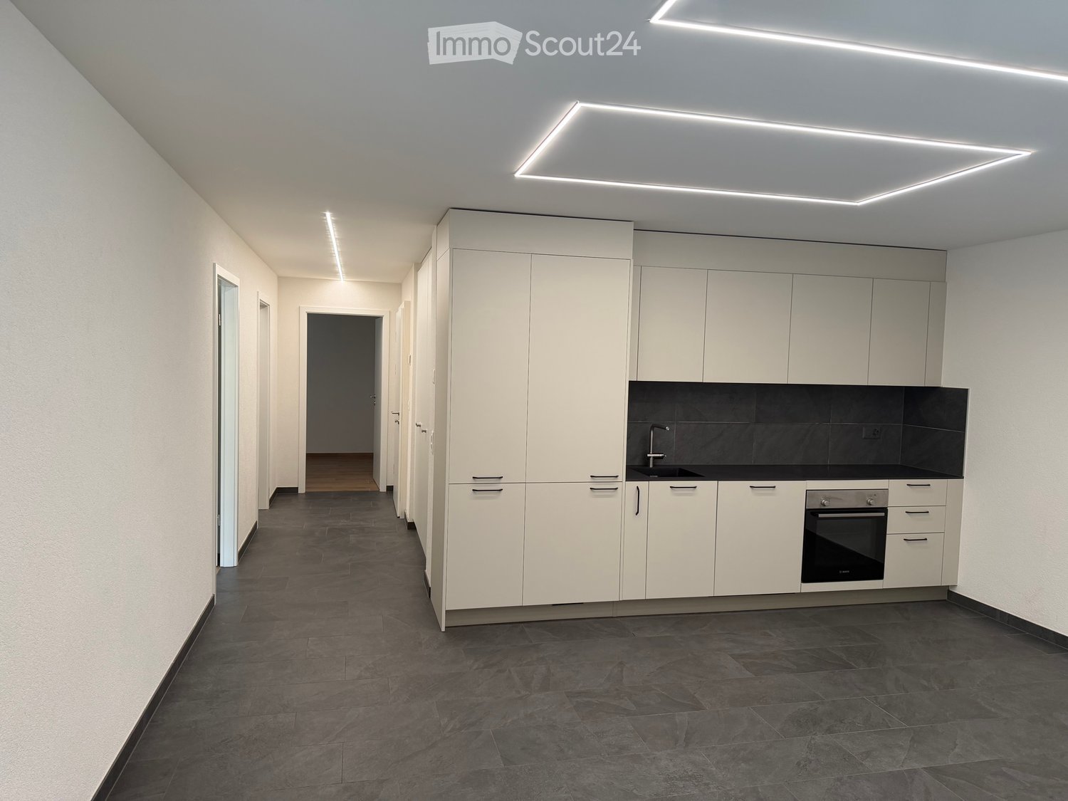 Modern kitchen with white cabinets, dark countertops, and built-in appliances including a sink and oven. The space features sleek, contemporary design with recessed lighting and a spacious layout.