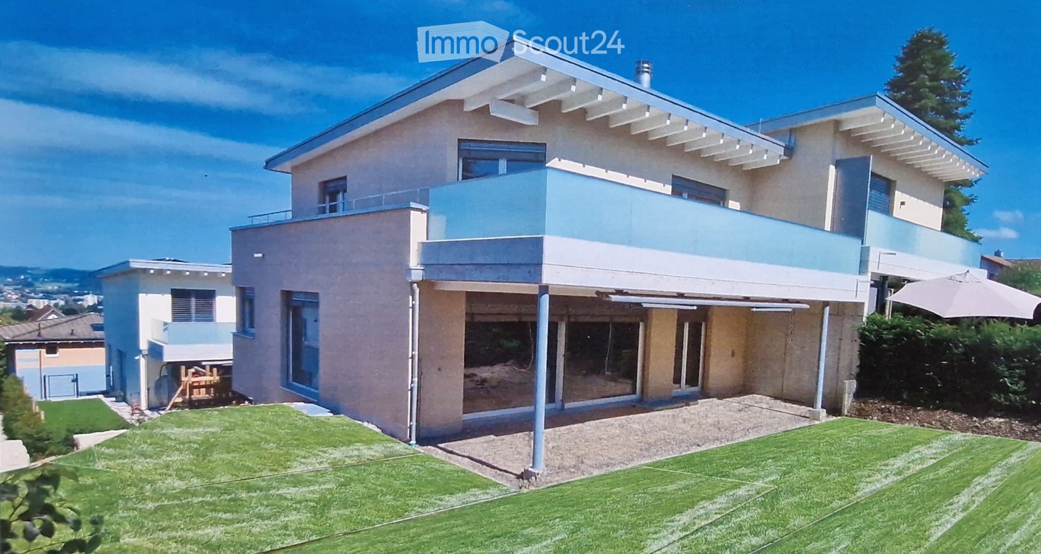 Modern two-story house with light-colored facade, large windows, and a spacious balcony overlooking the front yard.