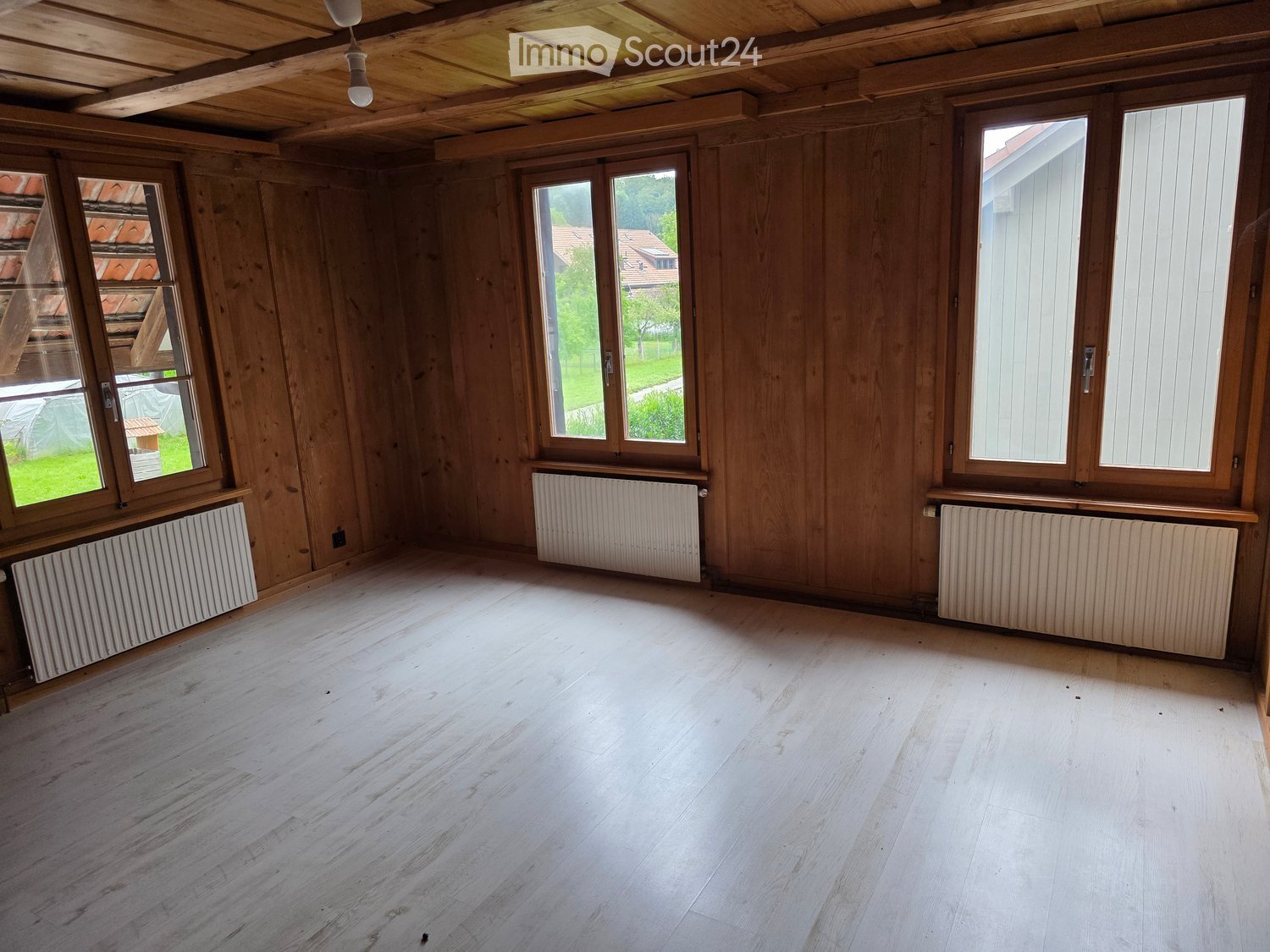 Empty room with wooden walls, wooden floor, and large windows with radiators beneath them.