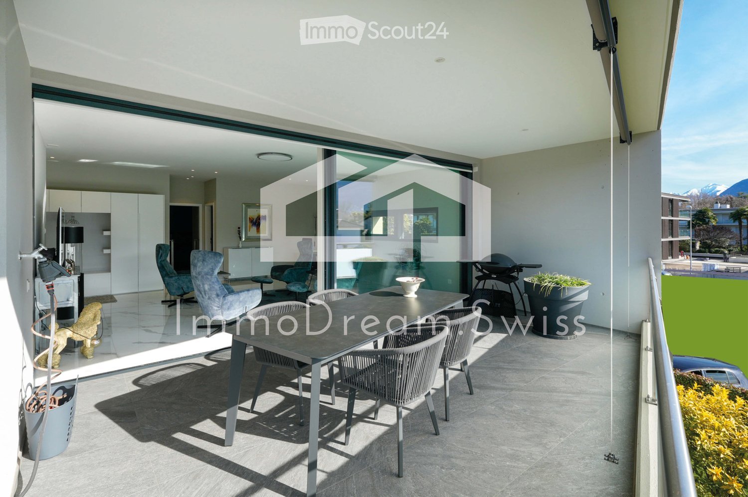 Modern balcony with a dining table, chairs, barbecue, and potted plants, offering a scenic mountain view.