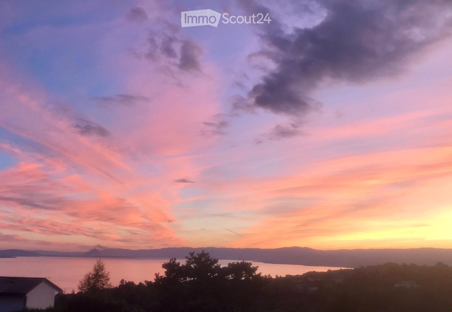 A serene sunset view over a body of water, with pink and orange hues in the sky and distant hills visible.