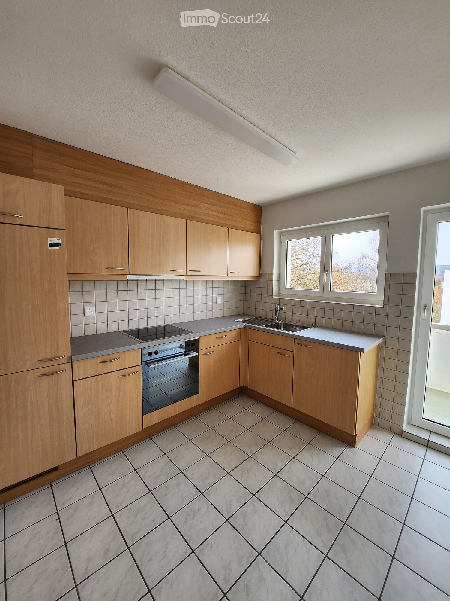 Modern kitchen with light wooden cabinets, stainless steel appliances, and tiled flooring.