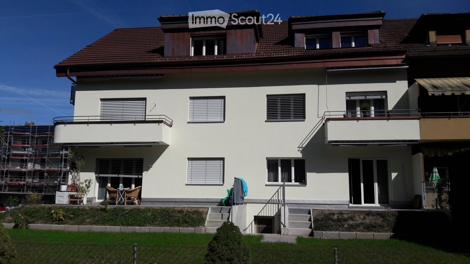 Two-story house with white exterior, multiple windows, balconies, and a small patio area with chairs and a table.