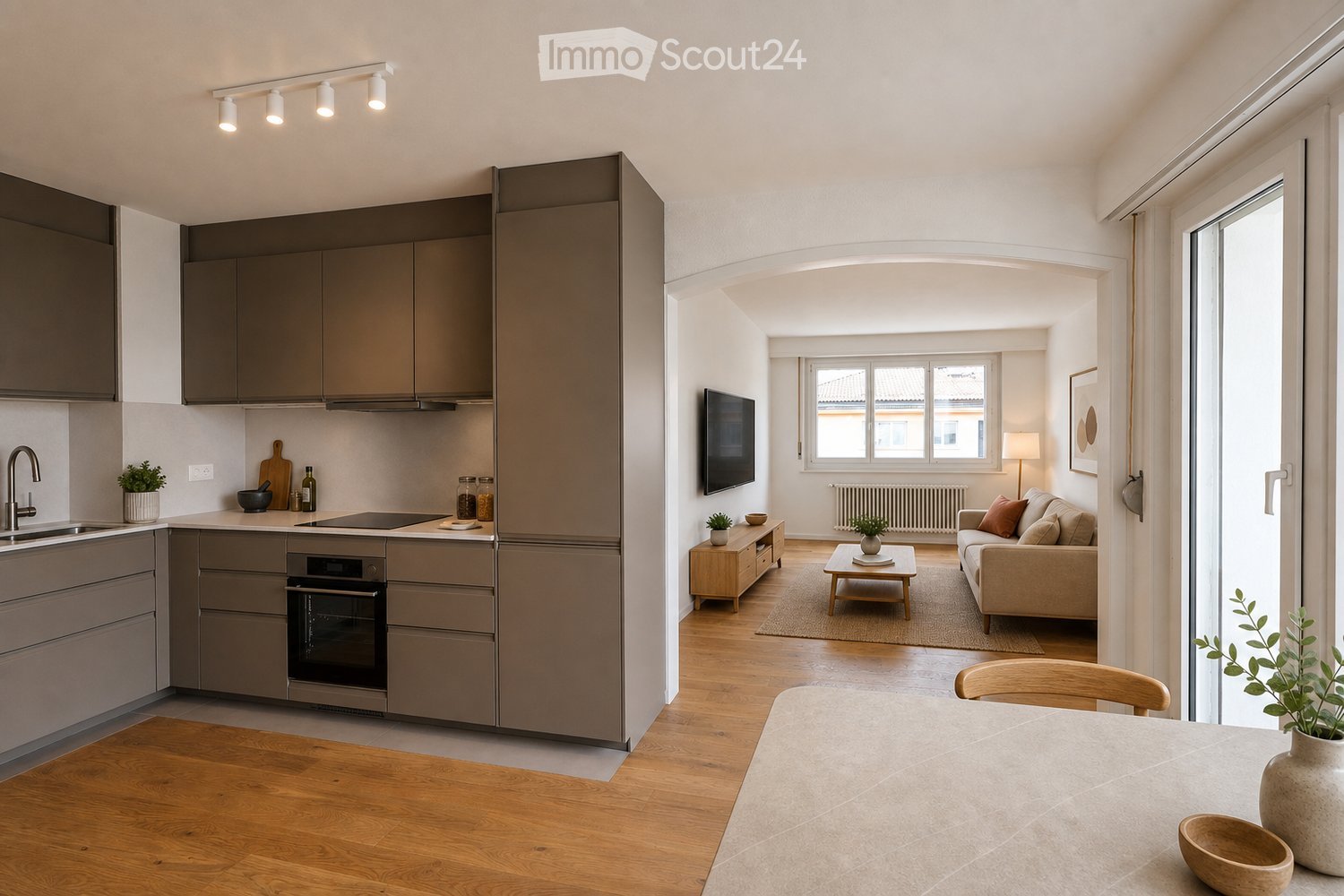 Modern open-plan living and dining area with a kitchen, featuring a sofa, coffee table, TV, and dining table with chairs. The kitchen includes an oven, sink, and faucet.