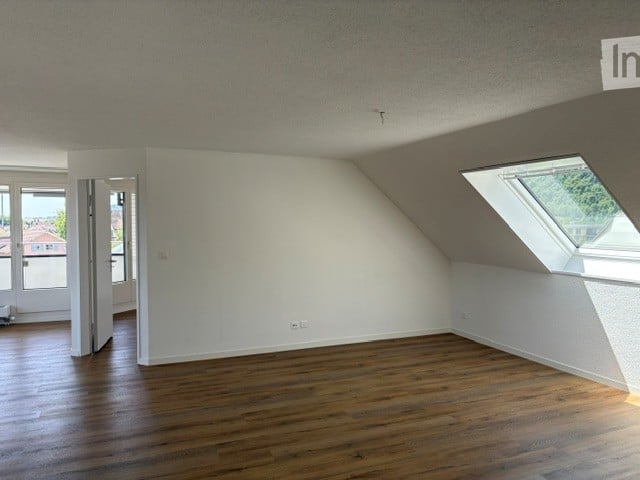 Completely empty room with wooden flooring, white walls, and large windows, including a skylight. No furniture or equipment.