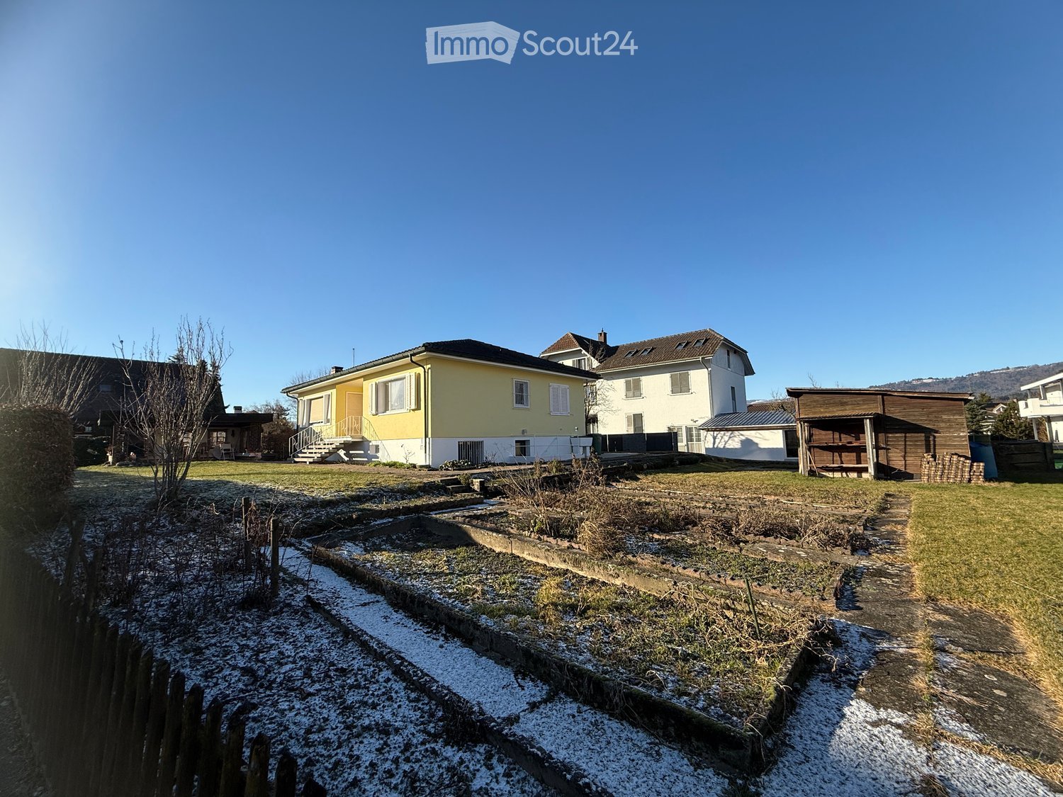 Two story house, yellow and white, chimney, garden with vegetable plots, and snow