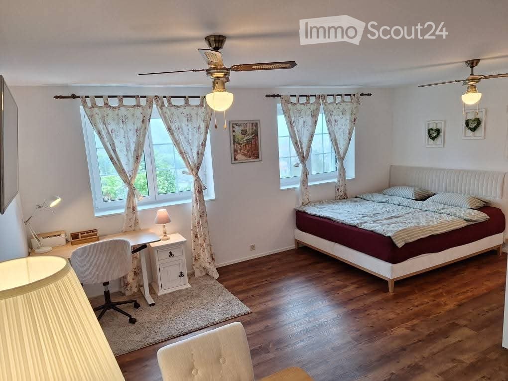 Cozy bedroom with wooden flooring, large bed with red and white bedding, desk with chair, and two ceiling fans with lights.